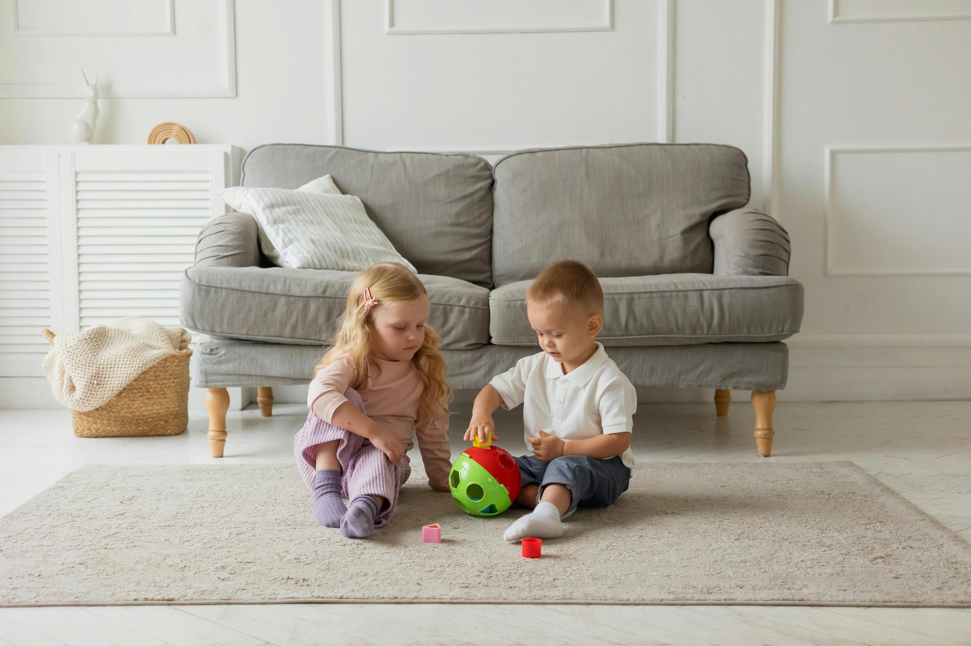 Two young children playing together on a rug in a calm, home-style room.